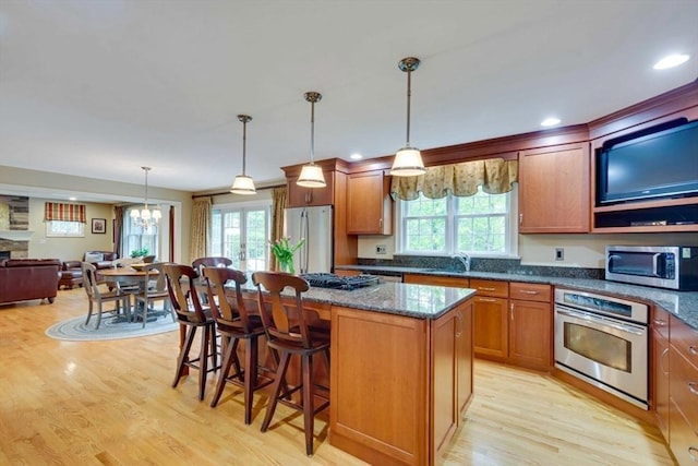 kitchen with stainless steel appliances, a sink, brown cabinetry, light wood finished floors, and a kitchen island
