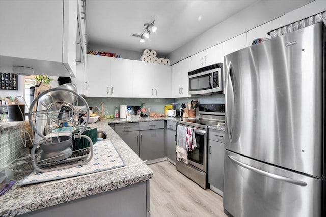 kitchen featuring light wood-type flooring, backsplash, gray cabinets, light stone counters, and appliances with stainless steel finishes