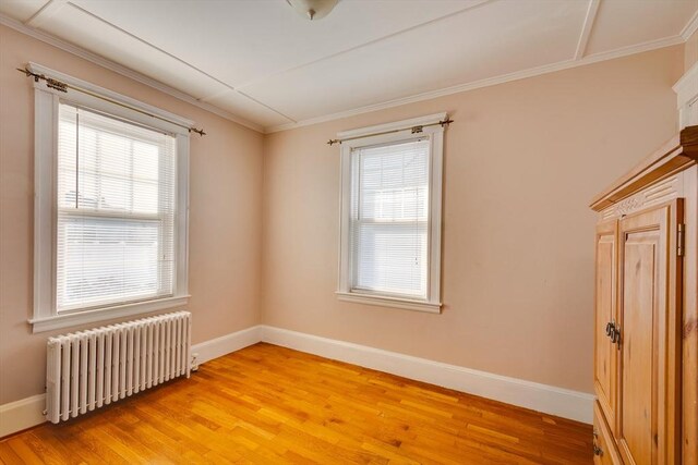 unfurnished room with a healthy amount of sunlight, radiator, crown molding, and light hardwood / wood-style flooring