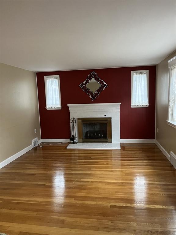 unfurnished living room with wood finished floors, a glass covered fireplace, visible vents, and baseboards