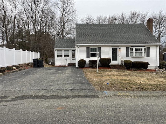 cape cod house with entry steps, a chimney, aphalt driveway, roof with shingles, and fence