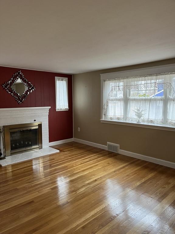 unfurnished living room with a fireplace, wood finished floors, visible vents, and baseboards