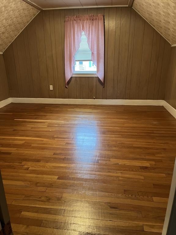 additional living space with vaulted ceiling, wood walls, and wood finished floors