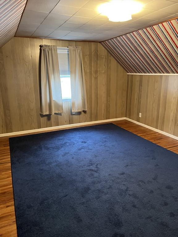 bonus room with carpet flooring, vaulted ceiling, wood walls, and baseboards