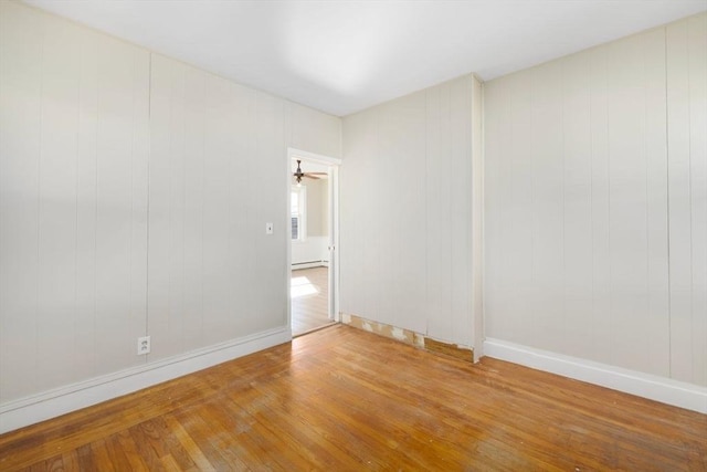 unfurnished room featuring wood-type flooring, a baseboard heating unit, and baseboards