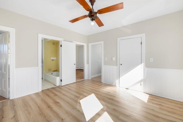 unfurnished bedroom featuring light wood-style floors, wainscoting, connected bathroom, and ceiling fan