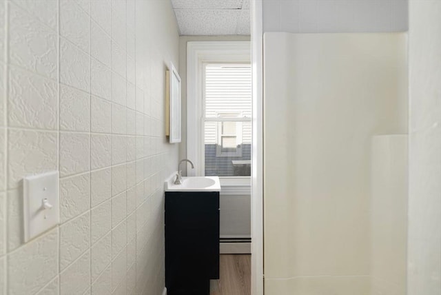 full bath with a baseboard radiator, wood finished floors, tile walls, and vanity