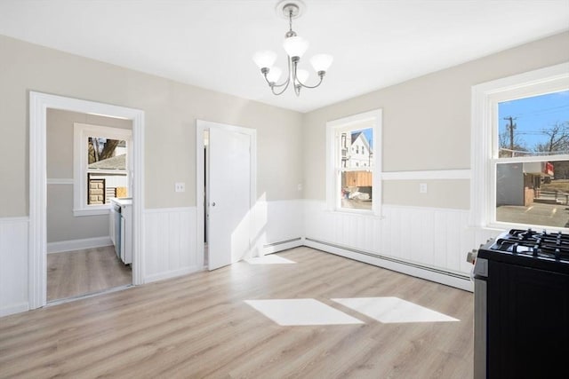 dining room with light wood-type flooring, a baseboard radiator, a wainscoted wall, and a notable chandelier