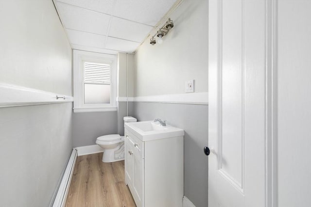 bathroom with baseboards, toilet, wood finished floors, baseboard heating, and vanity