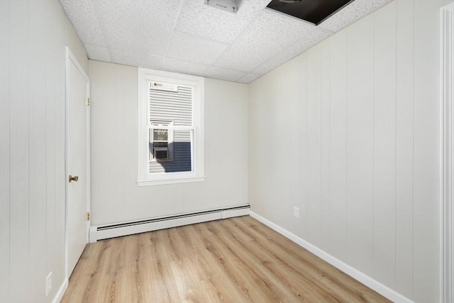 empty room with a drop ceiling, a baseboard radiator, wood finished floors, and baseboards