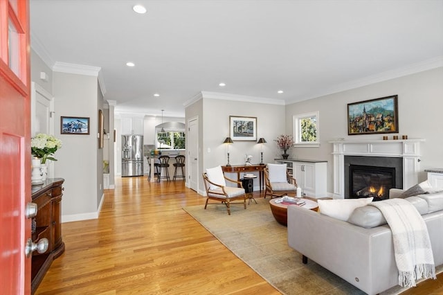 living area featuring recessed lighting, light wood-type flooring, a glass covered fireplace, and crown molding