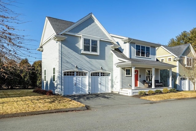 shingle-style home with covered porch, driveway, an attached garage, and a shingled roof