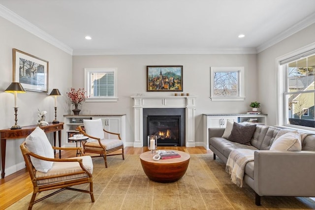 living area with baseboards, a glass covered fireplace, crown molding, and light wood finished floors