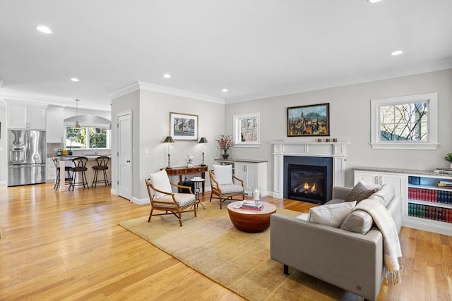 living room with baseboards, recessed lighting, a glass covered fireplace, crown molding, and light wood-type flooring