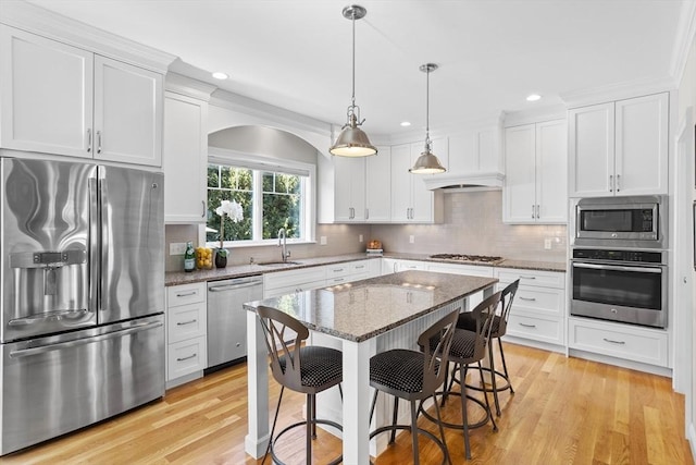 kitchen with white cabinetry, stainless steel appliances, a kitchen bar, and a sink