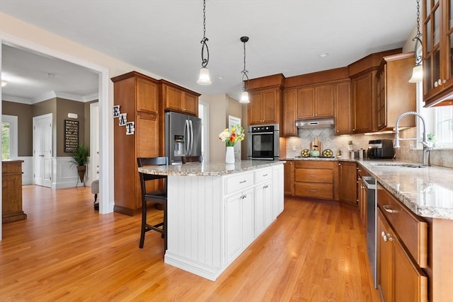 kitchen with a sink, stainless steel appliances, brown cabinets, under cabinet range hood, and light wood finished floors