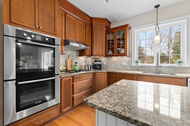 kitchen with under cabinet range hood, stainless steel appliances, brown cabinets, and a sink