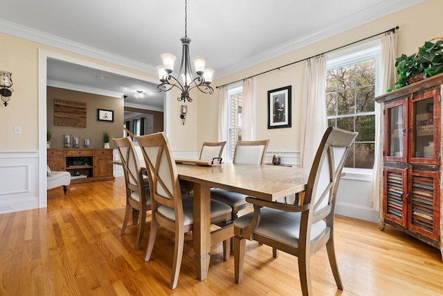 dining area with a decorative wall, an inviting chandelier, light wood-style flooring, crown molding, and wainscoting