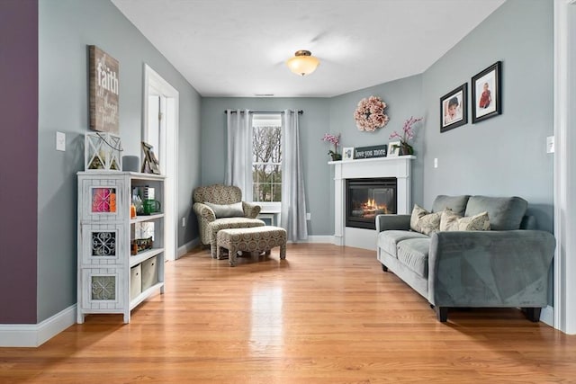 sitting room featuring baseboards, light wood-type flooring, and a glass covered fireplace