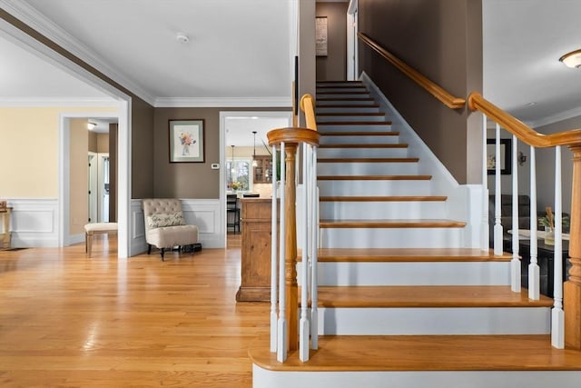 staircase featuring wainscoting, ornamental molding, a decorative wall, and wood finished floors