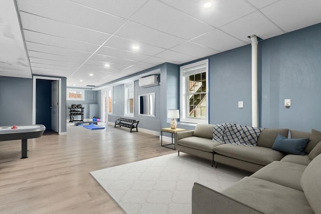 living area featuring light wood finished floors, a drop ceiling, baseboards, and an AC wall unit