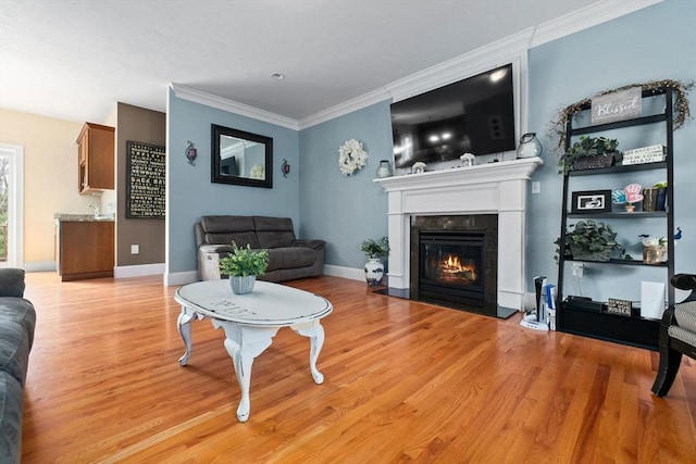 living room featuring baseboards, ornamental molding, light wood-type flooring, and a fireplace with flush hearth