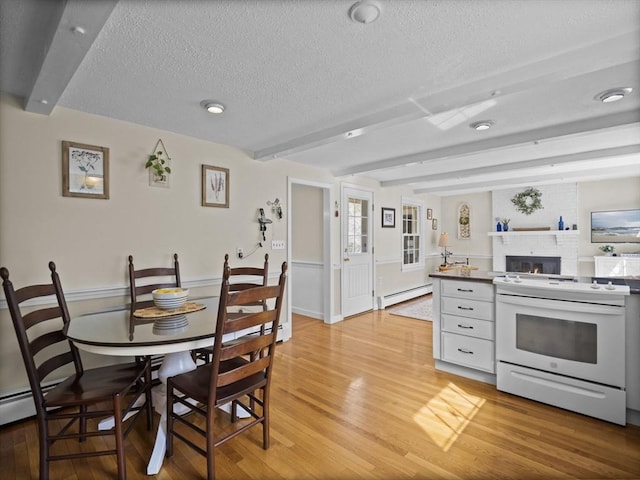 dining space featuring a brick fireplace, beam ceiling, baseboard heating, a textured ceiling, and light wood finished floors