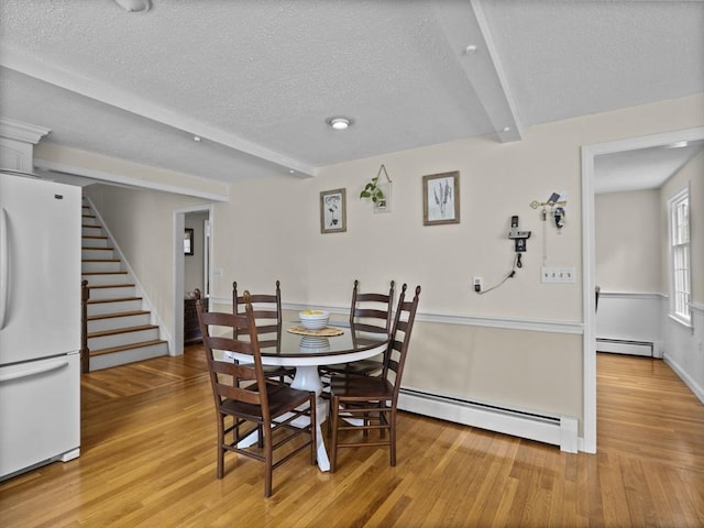 dining area with a baseboard heating unit, light wood finished floors, a textured ceiling, and stairs