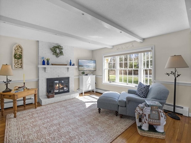 living area with a brick fireplace, beamed ceiling, baseboard heating, a textured ceiling, and hardwood / wood-style flooring