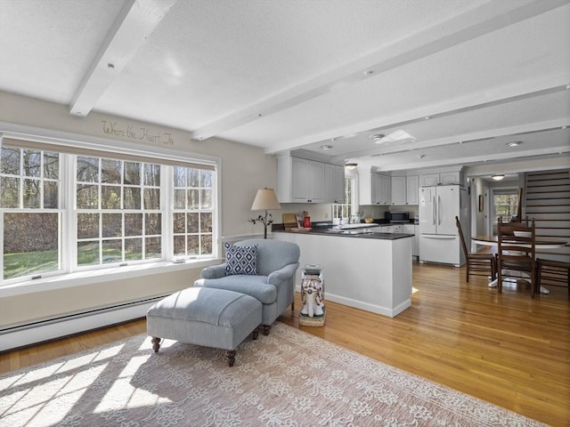 interior space with a textured ceiling, a baseboard heating unit, light wood finished floors, and beam ceiling