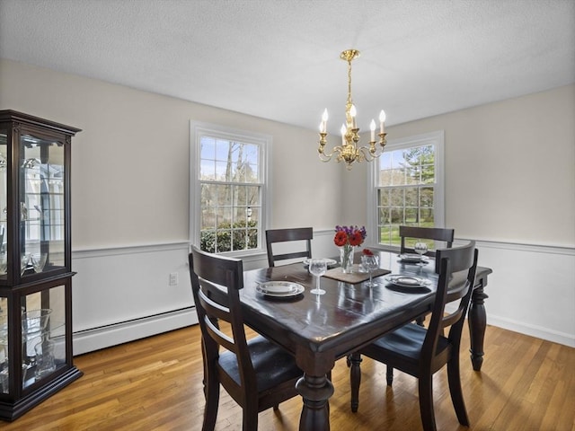 dining room featuring a baseboard heating unit, a textured ceiling, a notable chandelier, and wood finished floors
