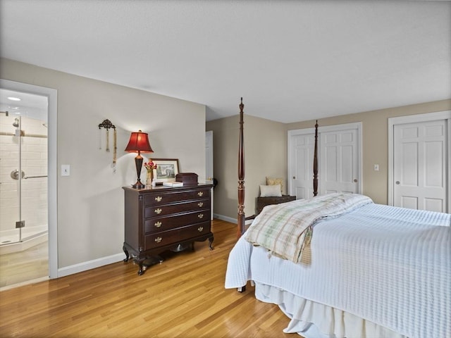 bedroom featuring baseboards, ensuite bathroom, two closets, and light wood-style flooring