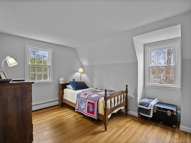 bedroom featuring baseboard heating, light wood finished floors, and lofted ceiling