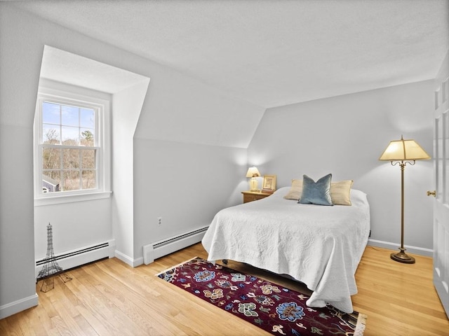 bedroom with a baseboard heating unit, wood finished floors, and lofted ceiling