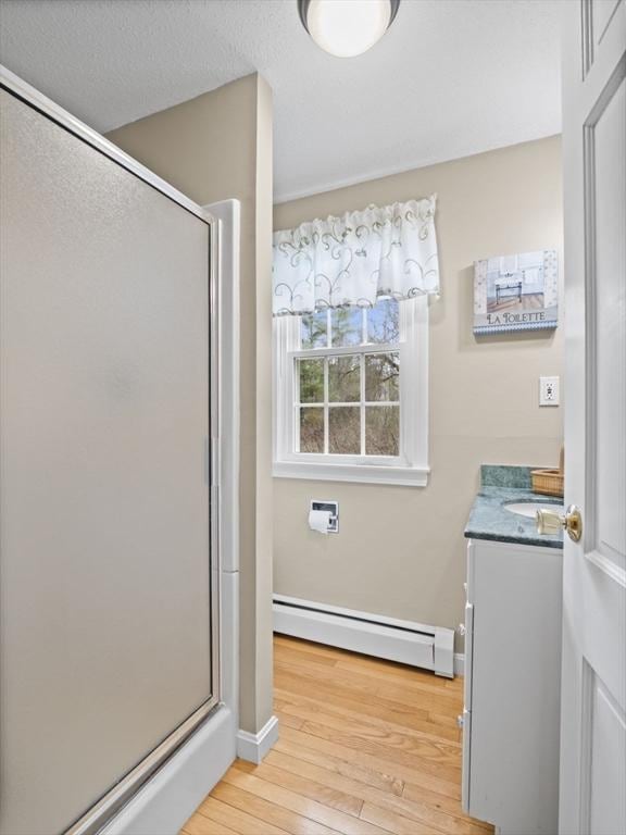 full bath featuring vanity, wood-type flooring, baseboards, a shower stall, and a baseboard heating unit