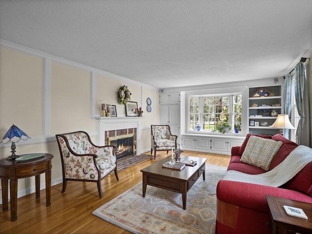 living area featuring a fireplace with flush hearth, a textured ceiling, ornamental molding, and wood finished floors
