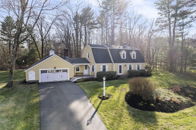 dutch colonial featuring driveway, a chimney, a gambrel roof, a front lawn, and an attached garage