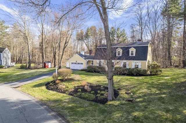 view of front facade featuring a garage, aphalt driveway, a front yard, a chimney, and a storage unit