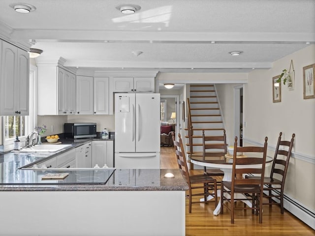 kitchen featuring light wood-type flooring, a sink, freestanding refrigerator, stainless steel microwave, and a peninsula