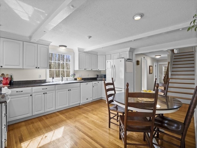 kitchen featuring a textured ceiling, light wood-type flooring, beam ceiling, a sink, and white appliances