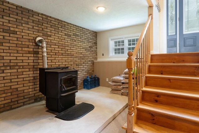 300 Henshaw St, Leicester, MA 01524 - carpeted living area with a wood stove, brick wall, stairs, a textured ceiling, and wainscoting