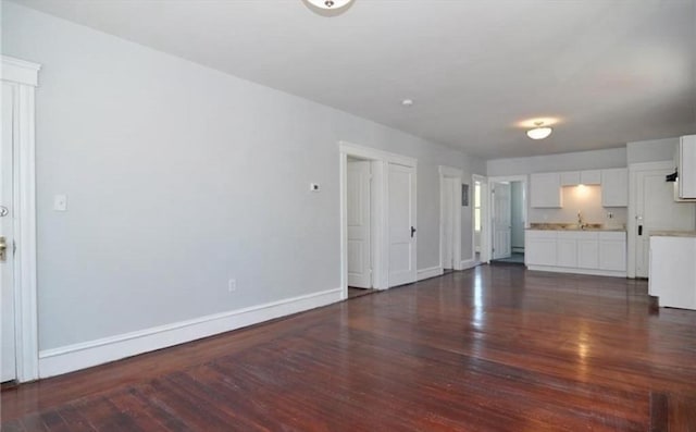 unfurnished living room with dark wood finished floors, baseboards, and a sink