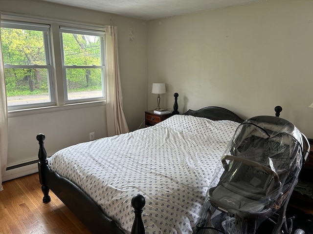 bedroom with hardwood / wood-style flooring, baseboard heating, and multiple windows