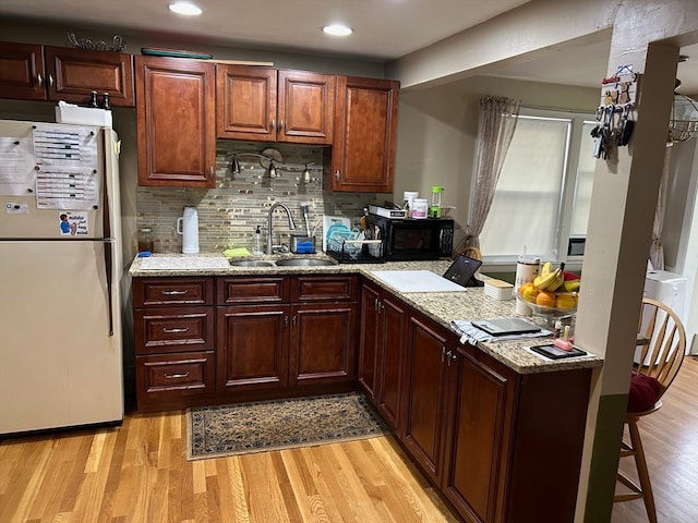 kitchen with light stone countertops, light hardwood / wood-style floors, tasteful backsplash, white fridge, and sink