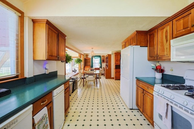 kitchen with an inviting chandelier, dark countertops, light floors, and white appliances