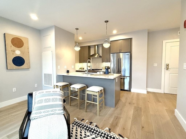 kitchen featuring wall chimney range hood, a breakfast bar, high end fridge, decorative light fixtures, and kitchen peninsula