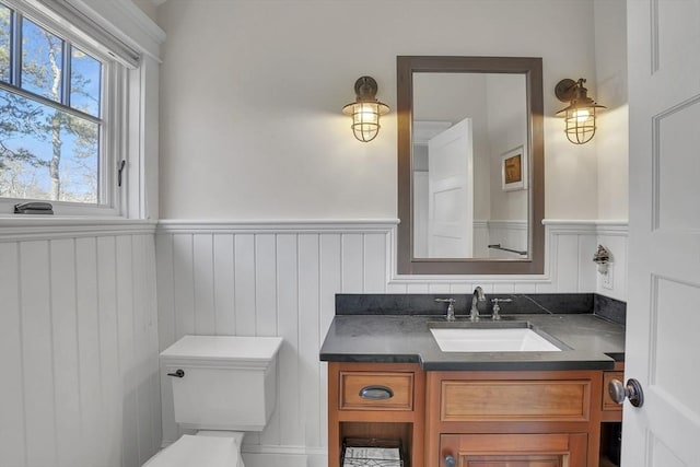 half bath with a wainscoted wall, vanity, and toilet