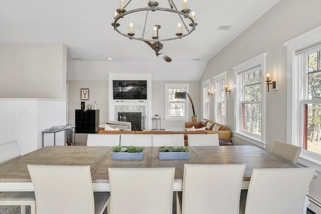 dining area featuring visible vents, a glass covered fireplace, baseboard heating, vaulted ceiling, and a chandelier