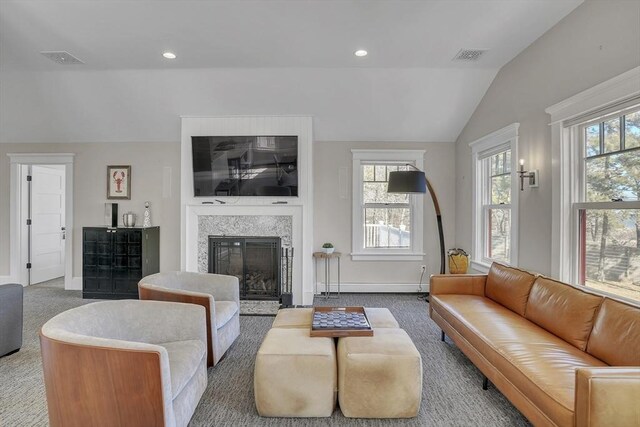 carpeted living area with vaulted ceiling, a glass covered fireplace, visible vents, and a healthy amount of sunlight