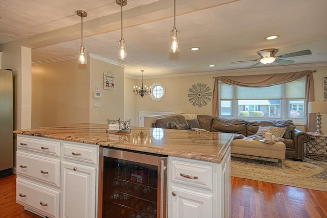 bar with ornamental molding, wood finished floors, beverage cooler, ceiling fan with notable chandelier, and hanging light fixtures